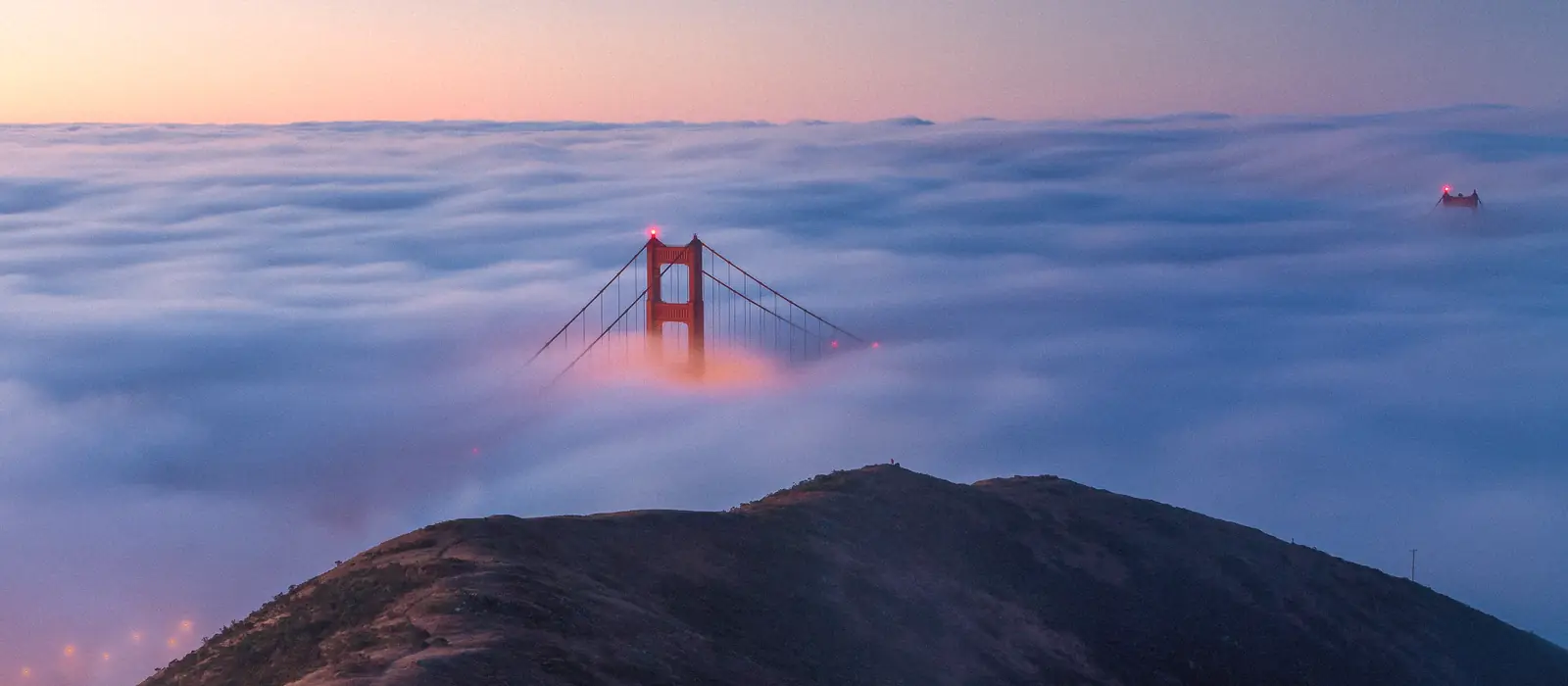 Photo of the Golden Gate Bridge towers above a sea of fog at dawn